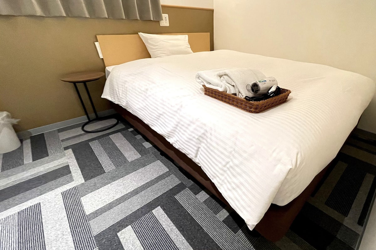 A hotel room with a neatly made bed, a small bedside table, and a patterned floor.