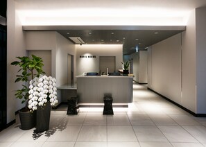 A modern hotel reception area with a reception desk, a potted plant, and a sign that reads "HOTEL NEXUS". - HOTEL NEXUS HakataSanno (Fukuoka)