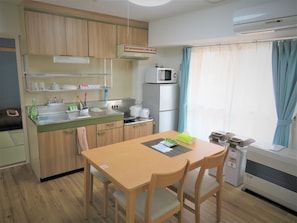 A compact kitchen with wooden cabinets, a microwave, a refrigerator, and a dining table with chairs. - Heights Showa 507 (Sapporo)