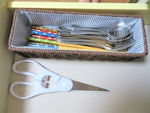 A wicker basket containing various utensils and a pair of scissors on a table.