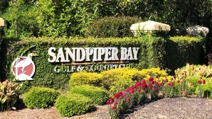 Naamplaatje voor Sandpiper Bay Golf & Country Club, omringd door keurig onderhouden hagen en kleurrijke bloemen.