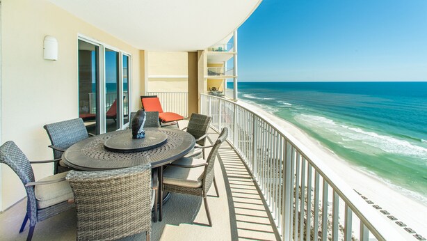 A balcony with a round table and chairs, overlooking the ocean.