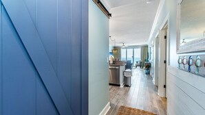 A hallway with a blue door, a kitchen area, and a dining area with a view.