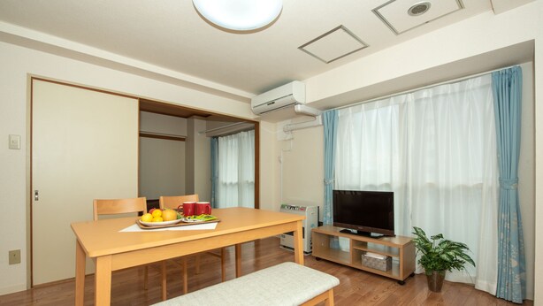 A modern living room with a wooden dining table, bench, TV, and potted plant. - Heights Showa 602 (Sapporo)