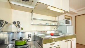 A kitchen with a green stove, white cabinets, a microwave, and a sink. - Heights Showa 602 (Sapporo)