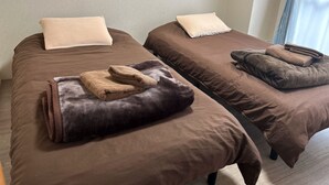 Two single beds with brown bedding and a beige pillow, a folded brown towel, and a window with curtains. - Heights Showa 602 (Sapporo)