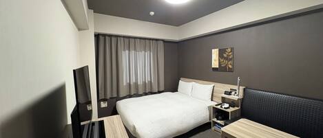 A hotel room with a bed, bedside table, TV, and a desk with a chair.