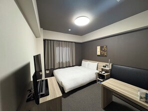 A hotel room with a bed, bedside table, TV, and a desk with a chair. - Hotel Route Inn Shinfuji Ekiminami (Fuji)