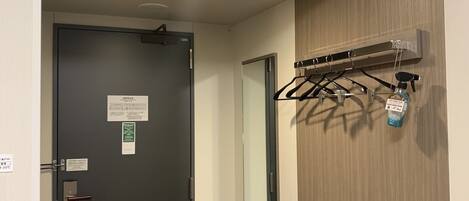 A hallway with a black door, an air conditioning unit mounted on the wall, and a coat rack with a spray bottle.