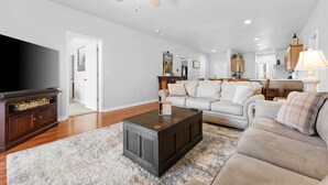 A living room with a dark wooden coffee table, a beige sofa, a television, and a ceiling fan. - Thousand Hills Golf View Condo Walkin w/ Elevator (Branson)