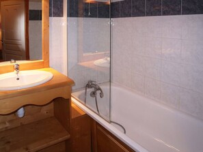 Un baño con tocador de madera, un lavabo blanco y zona de ducha con mampara de vidrio.