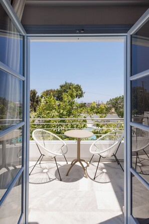 An open balcony with a table and two chairs, a clear view of the surrounding greenery and buildings. - Inoe Hotel (Santorini)