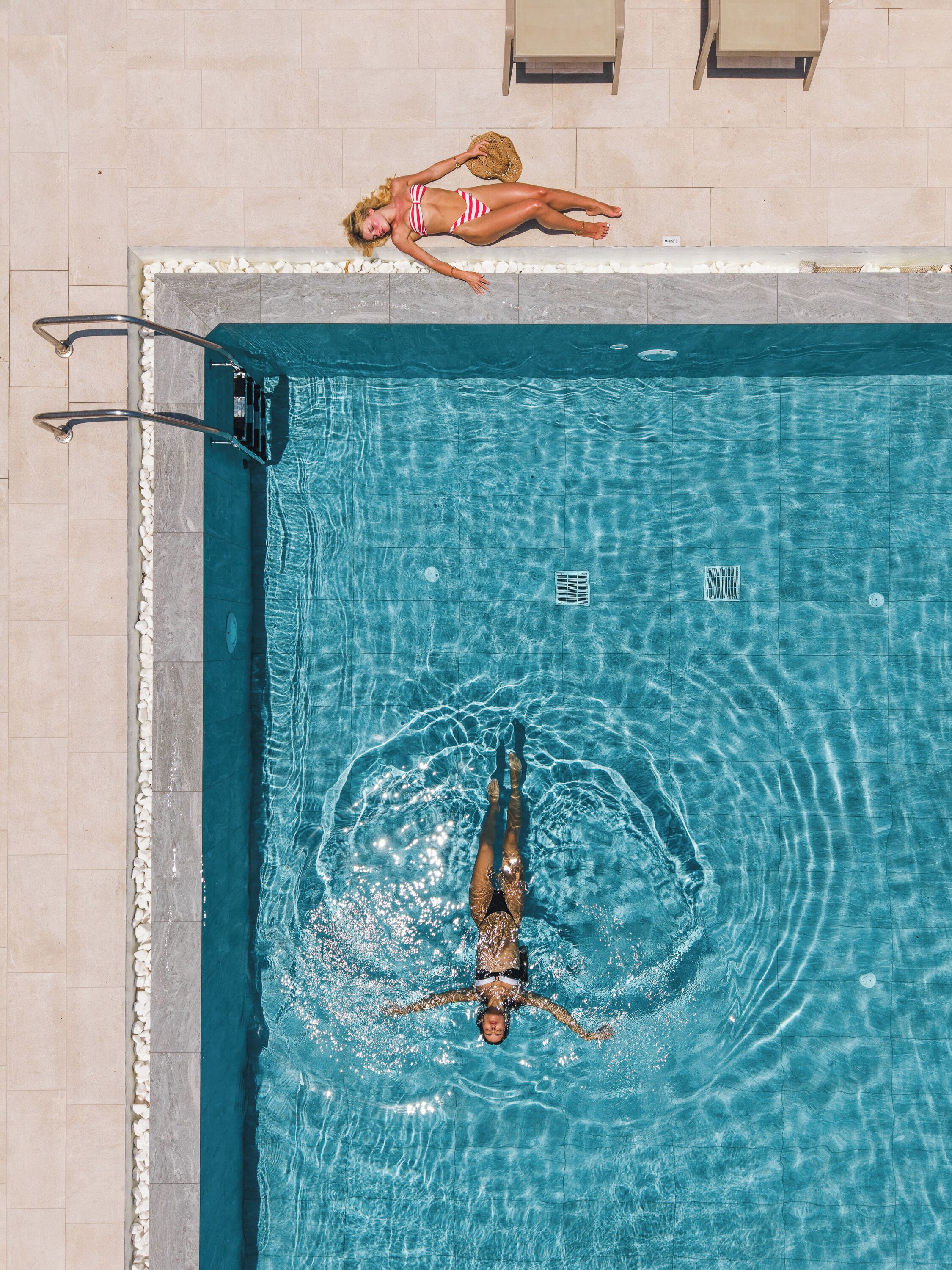 A swimming pool with clear water, a lifeguard stand, and a lounge area with chairs and a table.