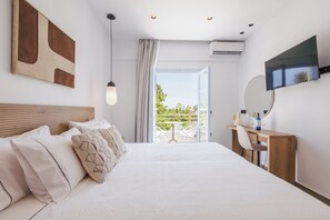 A hotel room with a bed, a desk, a chair, a TV, and a balcony with outdoor furniture. - Inoe Hotel (Santorini)