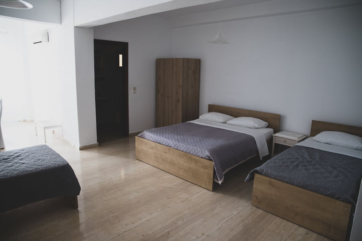 A bedroom with two beds, a wooden wardrobe, and a bedside table.