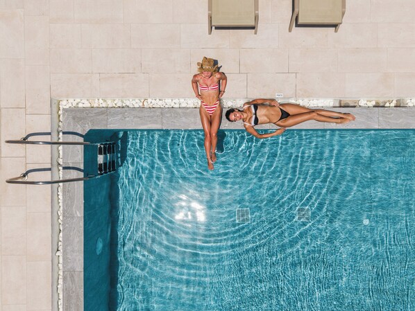 A swimming pool with two individuals, one standing and one lying on the edge. - Inoe Hotel (Santorini)