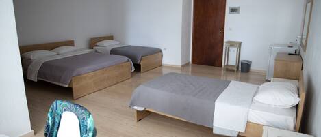 A room with two single beds, a wooden floor, a small table with a lamp, and a door.
