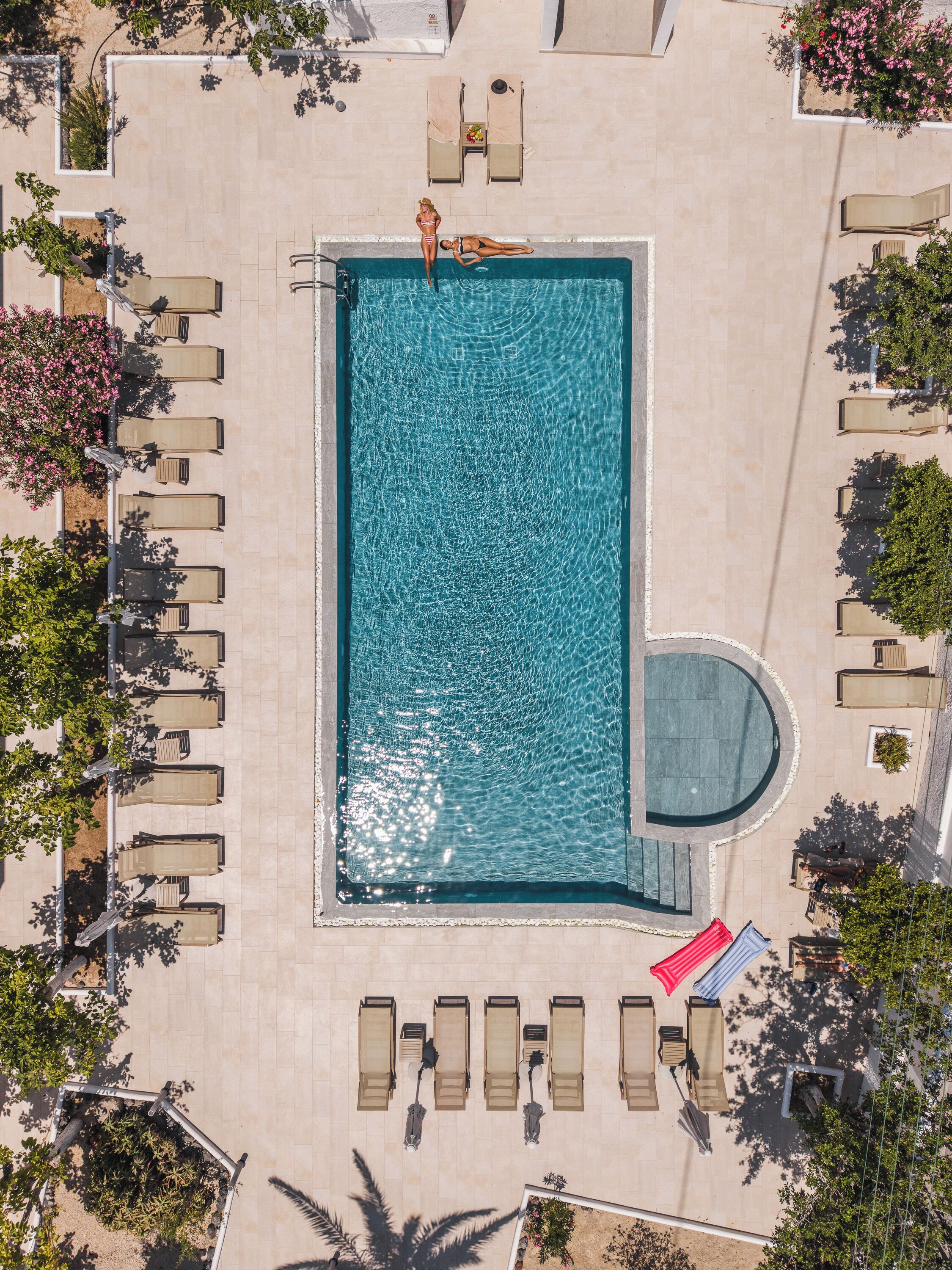 An aerial view of a rectangular swimming pool with a circular hot tub, surrounded by lounge chairs and potted plants.