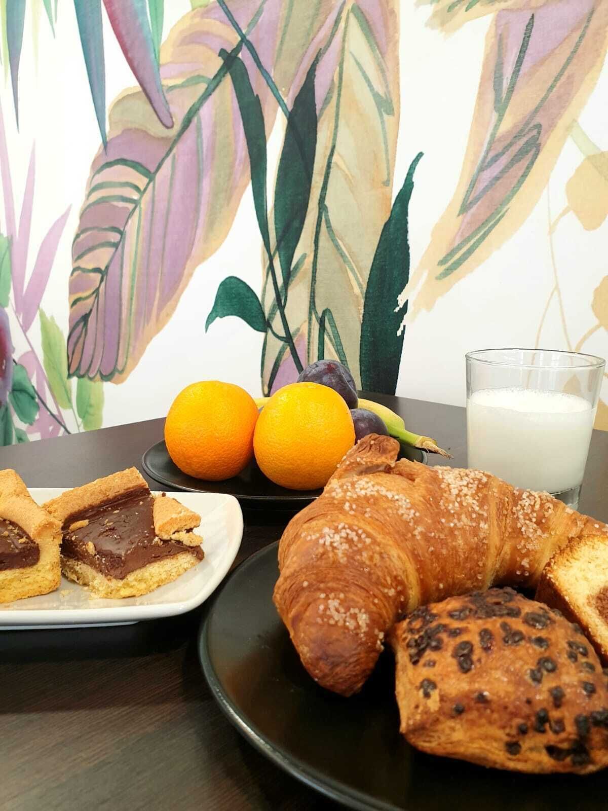 Une table mise pour le petit-déjeuner avec un croissant, des biscuits recouverts de chocolat, deux oranges et un verre de lait.