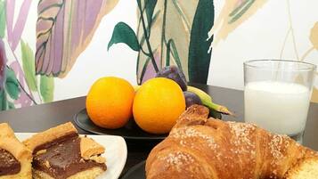 Une table mise pour le petit-déjeuner avec un croissant, des biscuits recouverts de chocolat, deux oranges et un verre de lait.