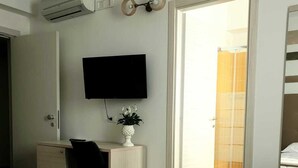 Una habitación de hotel con cama, escritorio, televisión y aire acondicionado.