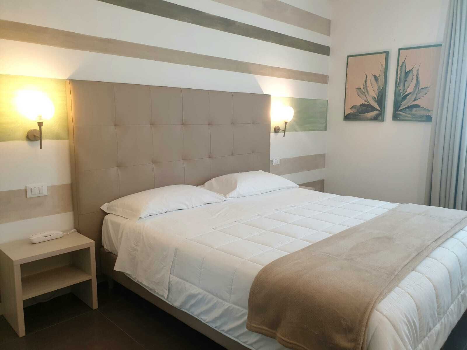 A neatly made bed with a headboard, a bedside table with a lamp, and two wall-mounted lights.