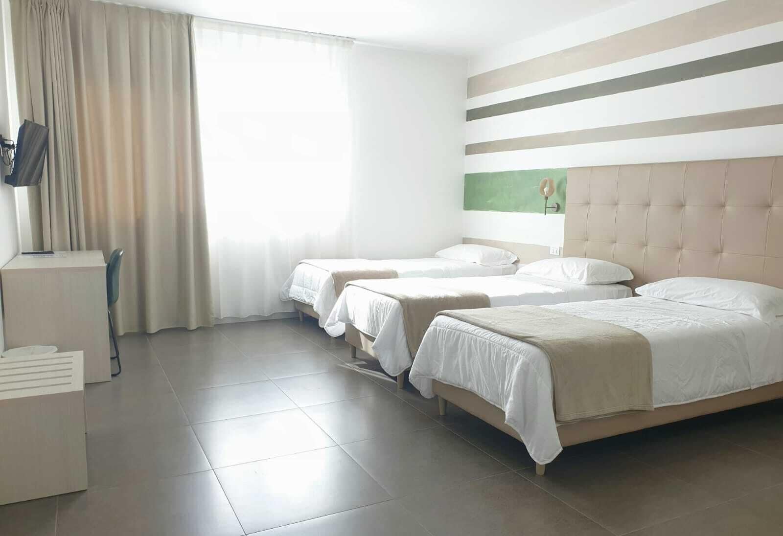 Ein Hotelzimmer mit drei Betten, einem Schreibtisch und einem Fernseher.