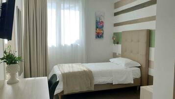 A neatly arranged hotel room with a bed, a chair, a table with a plant, a painting on the wall, and a window with curtains.