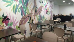 Un comedor moderno con un mural colorido, varias mesas y sillas.