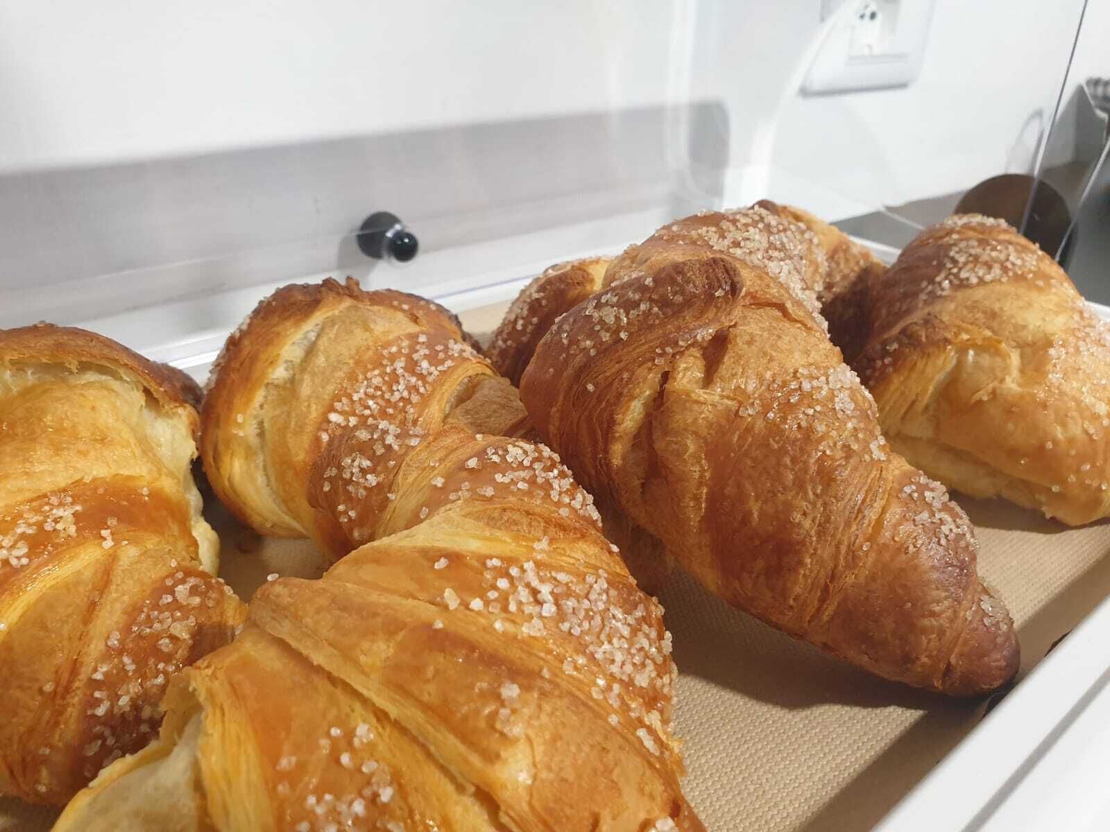 Una vitrina que contiene varios croissants dorados y crujientes, espolvoreados con sal.