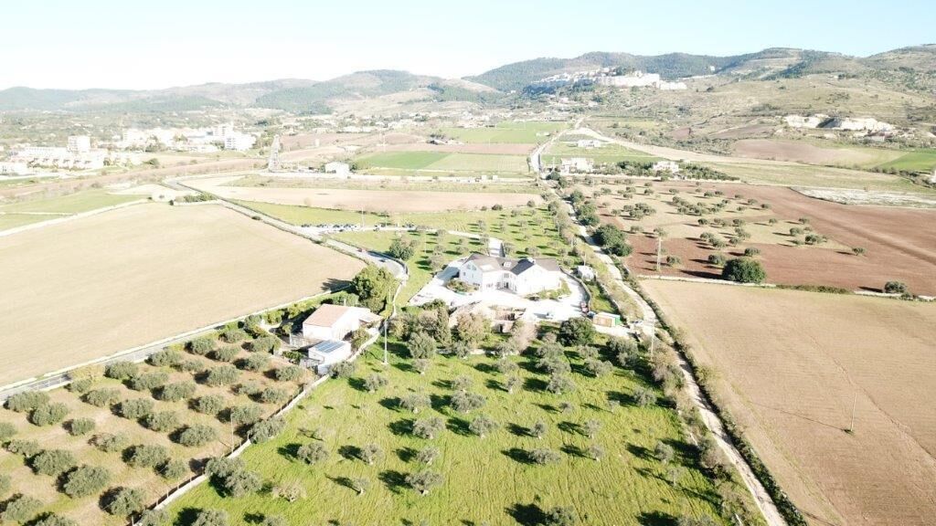 An aerial view of a rural landscape with fields, a few scattered buildings, and a large house surrounded by trees.