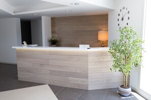 Un comptoir d’accueil avec un revêtement en bois, une horloge au mur et une plante en pot sur la droite.