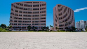 Two large, curved hotel buildings with multiple floors and balconies, surrounded by a sandy area with sparse vegetation. - Crescent Beach Club 3B Beachfront Views of the Gulf (Clearwater Beach)