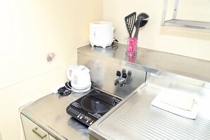 A kitchen with a stainless steel countertop, a coffee maker, a rice cooker, and a black induction cooktop.