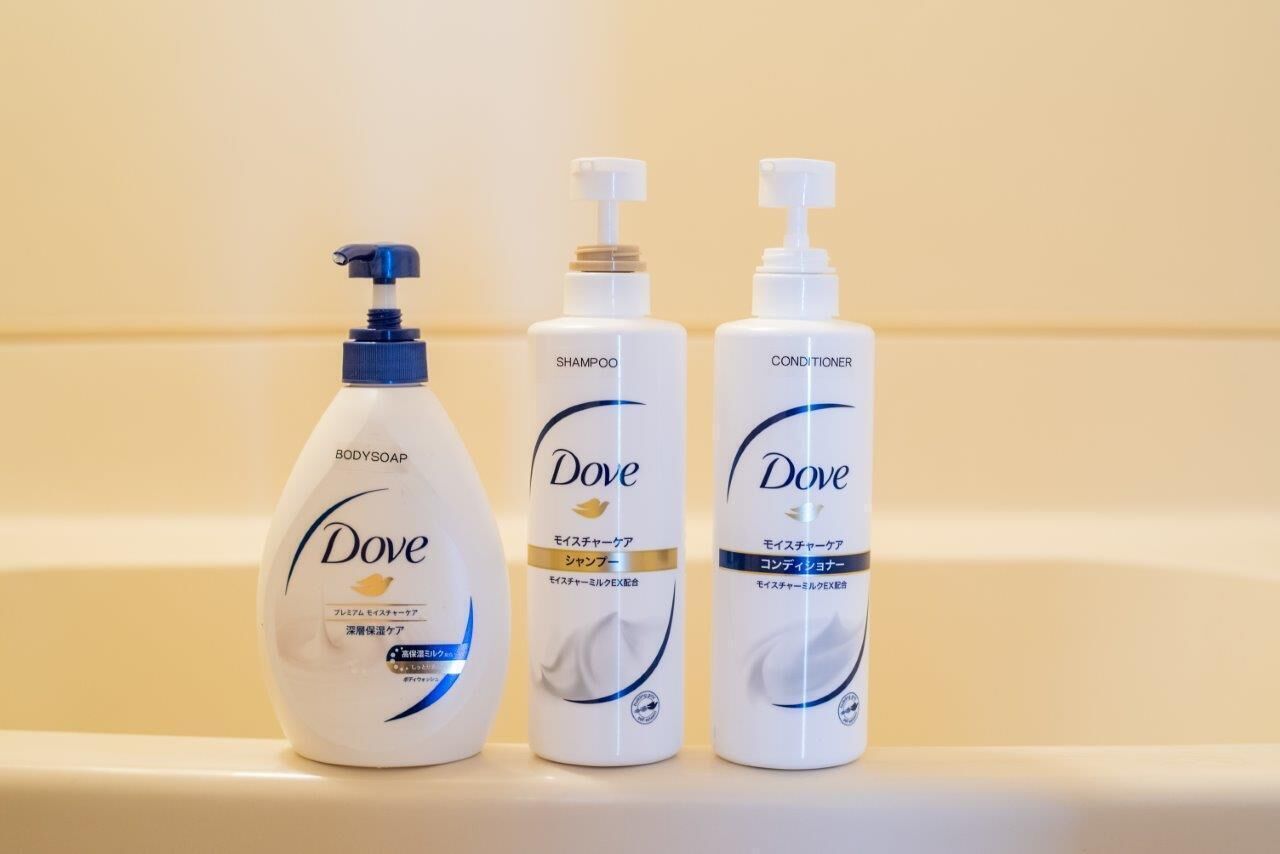 Tres productos para el cuidado corporal de Dove: jabón de baño, champú y acondicionador, sobre una estantería.
