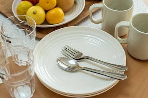 A dining setup with a white plate, forks, and a spoon on a wooden table.