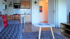 Um espaço de estar compacto com cozinha compacta, área de refeições e sala de estar com sofá e mesa redonda pequena.