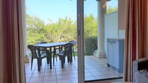Uma porta de correr de vidro dá acesso a um alpendre exterior com mesa e cadeiras, frigorífico e vista para o verde.