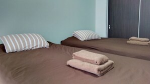 Two twin beds with brown bedding and striped pillows, a pair of folded towels on the bed, and a door in the background. - Heights Showa 703 (Sapporo)