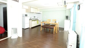 A modern kitchen with white cabinets, a microwave, and a dining area with a wooden table and chairs. - Heights Showa 703 (Sapporo)