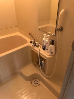 A bathroom with a bathtub, a sink, and a mirror. There are Dove body wash and lotion bottles on the sink.