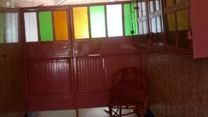 Una habitación con una puerta roja, una silla de madera y un ventanal con vidrios verdes y amarillos.