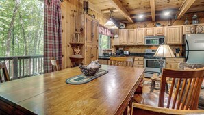 Une cuisine rustique aménagée dans une cabane en bois, avec une grande table à manger, des placards en bois et une vue sur la forêt par la fenêtre.