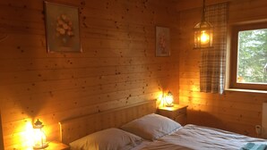 Een gezellig houten kamer met een bed, twee nachtkastjes, een raam met gordijnen en twee wandlampen.