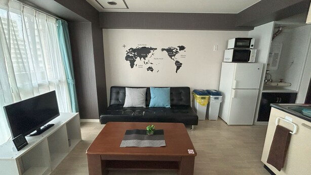 Ein kompakter Wohnbereich mit Sofa, Couchtisch, Fernseher, Küchenzeile und einer Weltkarte an der Wand.