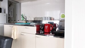 Eine moderne Küche mit weißen Schränken, einer Edelstahl-Arbeitsplatte, einem roten Wasserkocher und einer Kaffeemaschine.