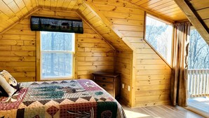 Ein gemütliches Schlafzimmer im Dachgeschoss mit holzgetäfelter Schräge, einem großen Fenster und einer gesteppten Bettdecke.