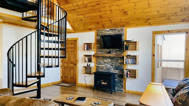 Ein gemütliches Wohnzimmer mit einer Holztreppe, einem Steinkamin, einem Flachbildfernseher und einer komfortablen Sitzecke.