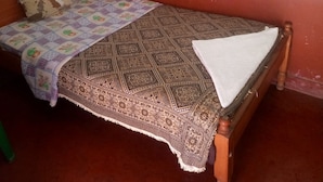 A single bed with a patterned bedspread and a white blanket, a wooden headboard, and a curtain on the window. - Kasambara Lodge (Naivasha)
