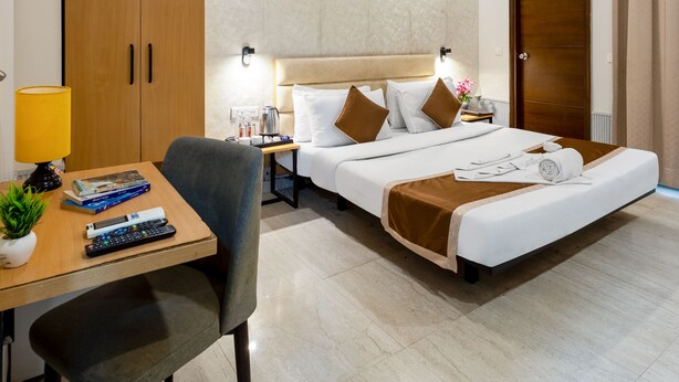 Une chambre d’hôtel comprenant un lit, un bureau avec une lampe, une chaise, une armoire et un ventilateur de plafond.